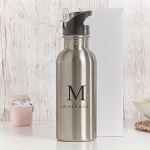 May include: A silver stainless steel water bottle with a black lid and a straw. The bottle has the letter "M" and the name "Melanie" engraved on it.