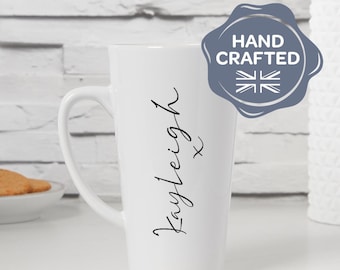 May include: A tall, white ceramic mug with a curved handle. The mug features the name "Kayleigh" in a handwritten font, with an "x" below. A "Hand Crafted" emblem is visible on the right side.