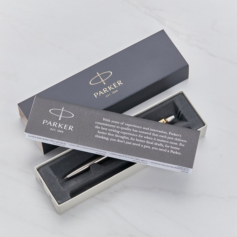 May include: A silver Parker pen with a gold trim in a white box with a black and white Parker logo and text that reads "With years of experience and innovation, Parker's commitment to quality has ensured that each pen delivers the best writing experience for when it matters most. For better first thoughts, for better final drafts, for better thinking, you don't just need a pen, you need a Parker."