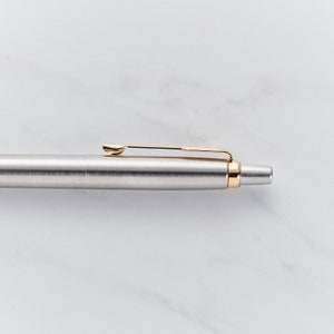 May include: A silver pen with a gold clip and a gold band near the tip.