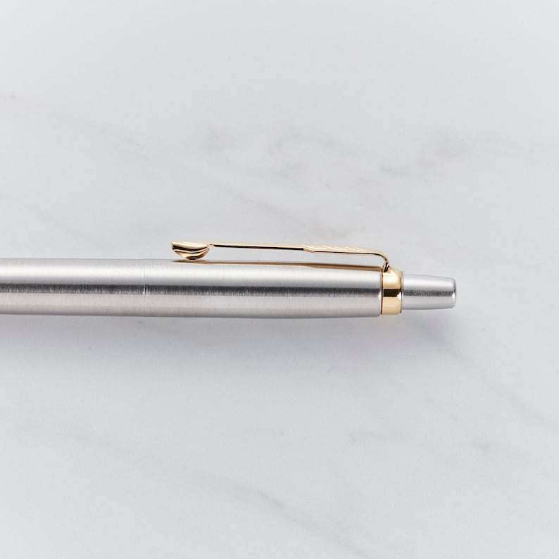 May include: A silver pen with a gold clip and a gold band near the tip.