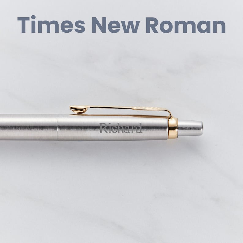 May include: A silver pen with a gold clip and a gold band at the end. The pen is engraved with the name "Richard" in a Times New Roman font.