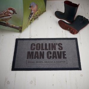 May include: Gray doormat with black text that reads "Collin's Man Cave Bring Beers, Snacks & Banter".