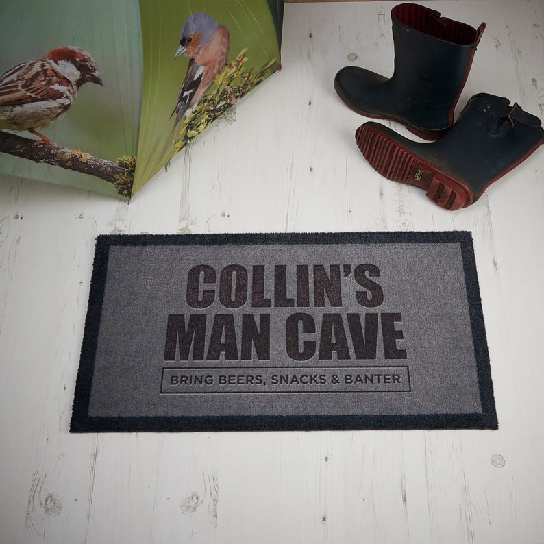 May include: Gray doormat with black text that reads "Collin's Man Cave Bring Beers, Snacks & Banter".