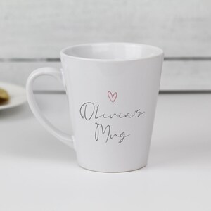 May include: White ceramic mug with a pink heart and the text "Olivia's Mug" in black cursive.