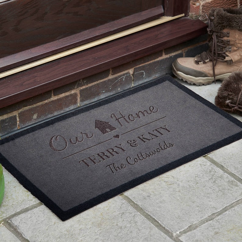 May include: A grey doormat with black edging and the text "Our Home Terry & Katy The Cotswolds" in a cursive font.