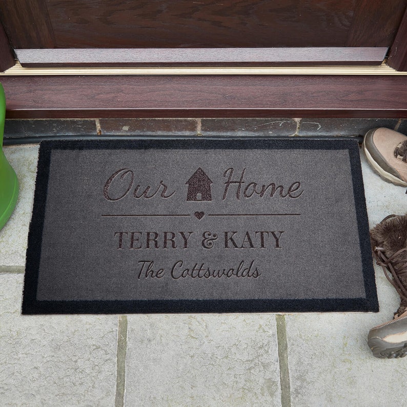 May include: A grey doormat with black edging featuring the text "Our Home" with a house icon, "Terry & Katy", and "The Cotswolds".