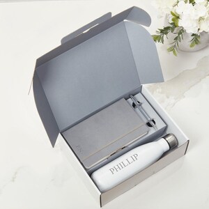 May include: A grey gift box containing a grey notebook, pen, and a white water bottle with the name "PHILLIP" engraved on it.