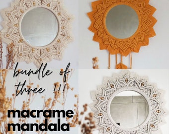 Peut inclure: Un lot de trois motifs de mandala en macramé. Les motifs sont de couleurs différentes, notamment beige, orange et blanc. Chaque motif présente un design circulaire avec un miroir central.