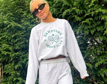 May include: Gray sweatshirt with a green graphic of tennis rackets and the text "HAMPTONS 19 87 TENNIS CLUB". The sweatshirt is paired with matching gray sweatpants.