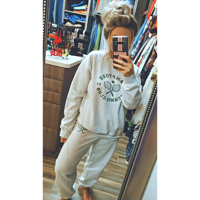 May include: A gray sweatshirt with a green tennis racket graphic and the text "Tennis Club" in a circle. The sweatshirt is paired with matching gray sweatpants.