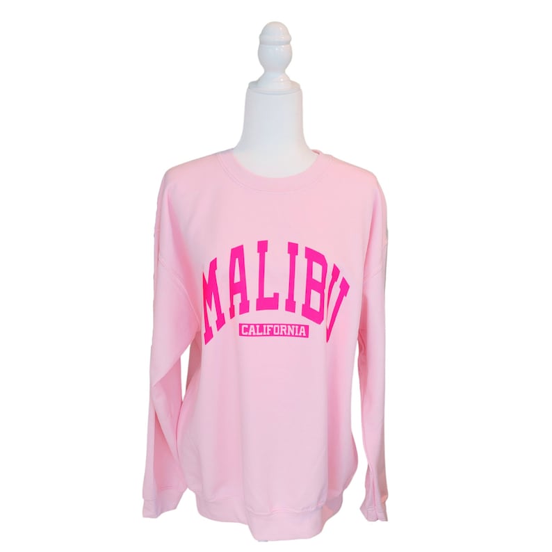 Op de afbeelding: Roze sweatshirt met een roze "MALIBU CALIFORNIA" afbeelding.