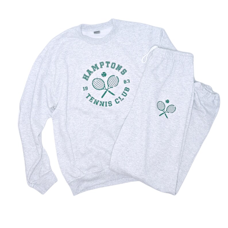 May include: Gray sweatshirt and sweatpants set with a green tennis racket and ball graphic. The sweatshirt has the text "HAMPTONS TENNIS CLUB 19 83" around the graphic. The sweatpants have a smaller version of the graphic on the left leg.