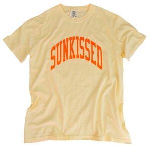 May include: A yellow t-shirt with an orange arch design that says "SUNKISSED".