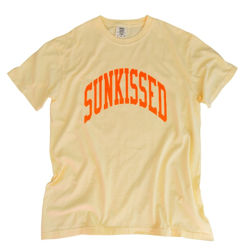 Puede incluir: Una camiseta de color amarillo p&aacute;lido con un dise&ntilde;o de arco naranja que dice "SUNKISSED".