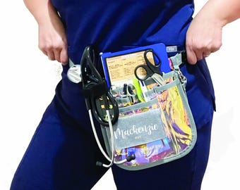 May include: A gray and iridescent medical utility belt with multiple pockets, holding a stethoscope, scissors, pens, and a clipboard. The belt is personalized with the name "Mackenzie" and the initials "RVT".