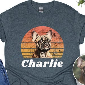 Dark heather gray unisex t-shirt featuring a custom pet portrait of a French bulldog inside a retro sunset circle graphic, with the name “Charlie” printed in large distressed white letters across the front. Casual short-sleeve crewneck tee with centered personalized dog design for pet lovers.