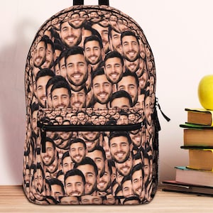 May include: A personalized backpack covered in a repeating pattern of smiling faces. The backpack has a black handle and zipper, with a front pocket. A stack of books, a yellow apple, and a clock are in the background.