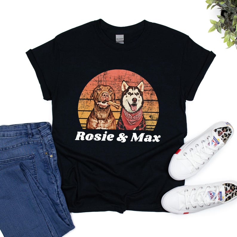 Graphic t-shirt featuring a pitbull and husky portrait with the names in bold, white, distressed font below. The dog image is placed inside a vintage-style, sunset-colored circle, blending shades of orange, yellow, and red for a retro aesthetic.
