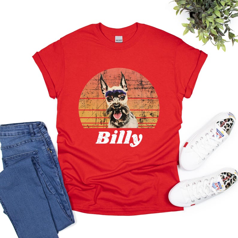Graphic t-shirt featuring a dog portrait with the name in bold, white, distressed font below. The dog image is placed inside a vintage-style, sunset-colored circle, blending shades of orange, yellow, and red for a retro aesthetic.