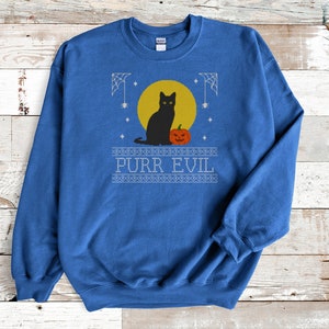 May include: A royal blue crewneck sweatshirt featuring a graphic print of a black cat sitting next to an orange jack-o'-lantern in front of a yellow full moon. The design includes white spiderwebs, stars, and the text PURR EVIL in a block font.