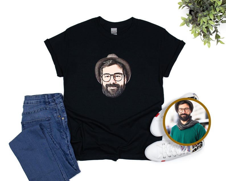 May include: Black t-shirt with a portrait of a man wearing glasses, a hat, and a beard. The image is paired with blue jeans and white trainers. A circular image of the man is also present, showing a green scarf.