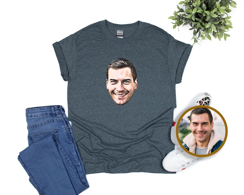 May include: A dark grey t-shirt with a smiling face graphic. The shirt is styled with blue jeans and white trainers with a leopard print design. A circular photo of the face is also included.