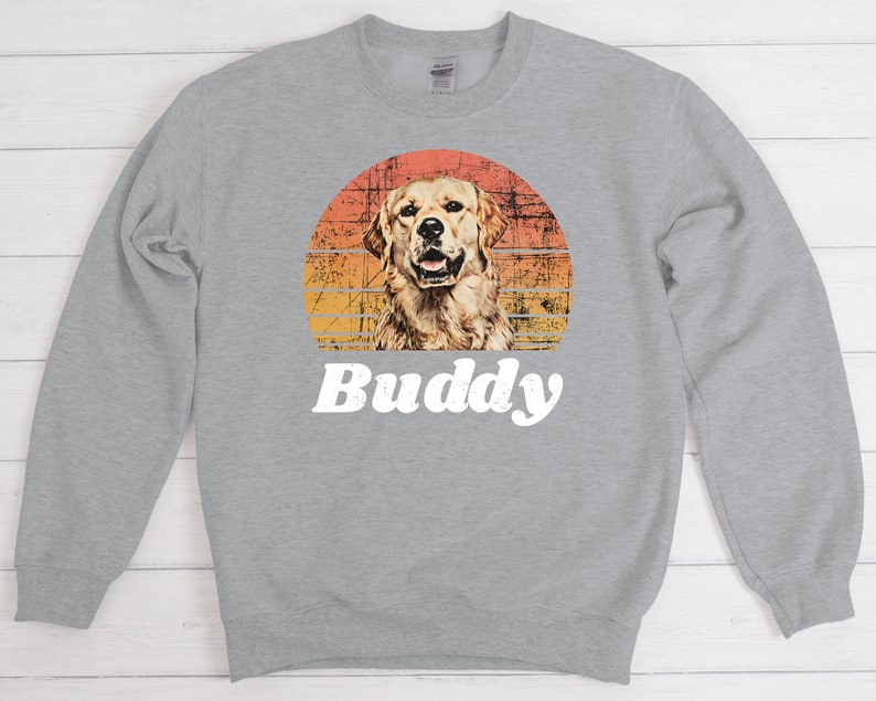 May include: A gray sweatshirt with a retro sunset graphic featuring a golden retriever dog. The text "Buddy" is printed below the graphic.