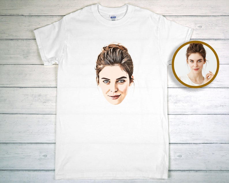 May include: White t-shirt with a printed portrait of a woman with brown hair and blue eyes. A smaller, circular image of the same portrait is in the upper right corner. The t-shirt is made of a white fabric.