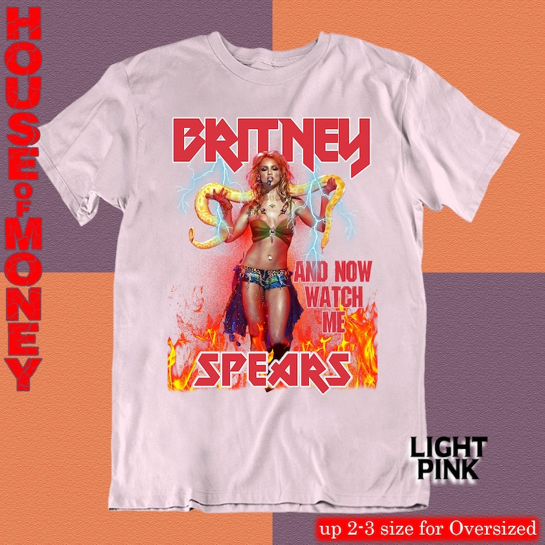 May include: Light pink t-shirt featuring a graphic of Britney Spears with the text "BRITNEY SPEARS" in red. The design includes an image of Britney holding a snake, with the words "AND NOW WATCH ME" in white. The shirt is labeled "LIGHT PINK".