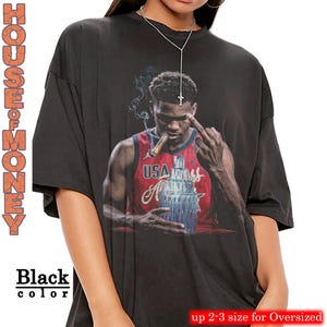 May include: Black oversized t-shirt featuring a graphic of a basketball player smoking a cigar and holding a trophy. The shirt has the text "HOUSE OF MONEY" and "Black color" printed on it. The shirt is available in up to 2-3 sizes for an oversized fit.
