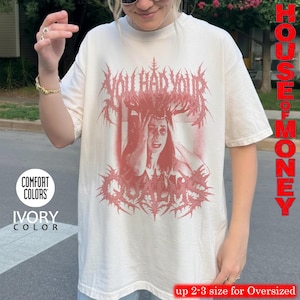 May include: An ivory-colored short-sleeve t-shirt featuring a red graphic print of a person with hands on their head, surrounded by spiky, metal-style lettering that reads "YOU HAD YOUR QUALMS." The shirt includes a Comfort Colors brand label.