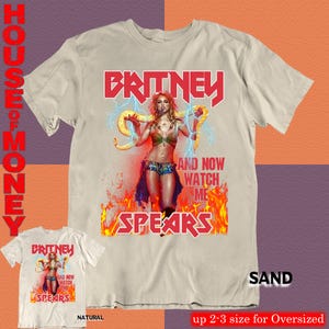 May include: Sand-colored t-shirt featuring a graphic of Britney Spears with the text "BRITNEY" in red, and "AND NOW WATCH ME SPEARS". A smaller, natural-colored shirt with the same design is also shown.