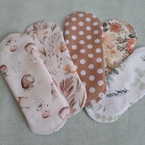 Könnte beinhalten: Sechs wiederverwendbare Stoffpads mit verschiedenen Mustern. Die Muster umfassen einen braunen und weißen Punkt, ein Blumenmuster mit rosa und gelben Blumen, ein Blattmuster mit grünen Blättern und ein Muster mit kleinen Tieren und Pflanzen.