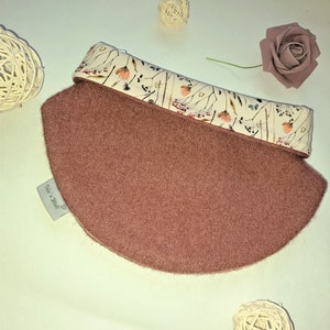 Könnte beinhalten: Ein runder, weicher, mauvefarbener Fleece-Halswärmer mit einem weißen Stoffbesatz mit floralem Muster. Der Stoffbesatz hat ein kleines Etikett mit der Aufschrift "Made with love".