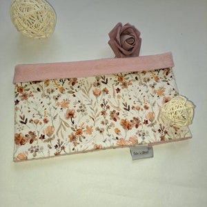 Könnte beinhalten: Eine kleine, rechteckige Tasche mit einem Blumendruck in Braun-, Orange- und Weißtönen. Die Tasche hat ein rosa Stofffutter und ein kleines Etikett mit der Aufschrift "Ida's World".
