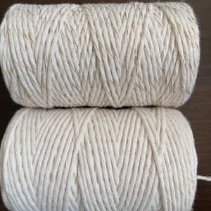 K&ouml;nnte beinhalten: Zwei Spulen aus nat&uuml;rlichem Baumwollseil. Die obere Spule hat einen goldenen Faden, der in das Seil eingewebt ist.