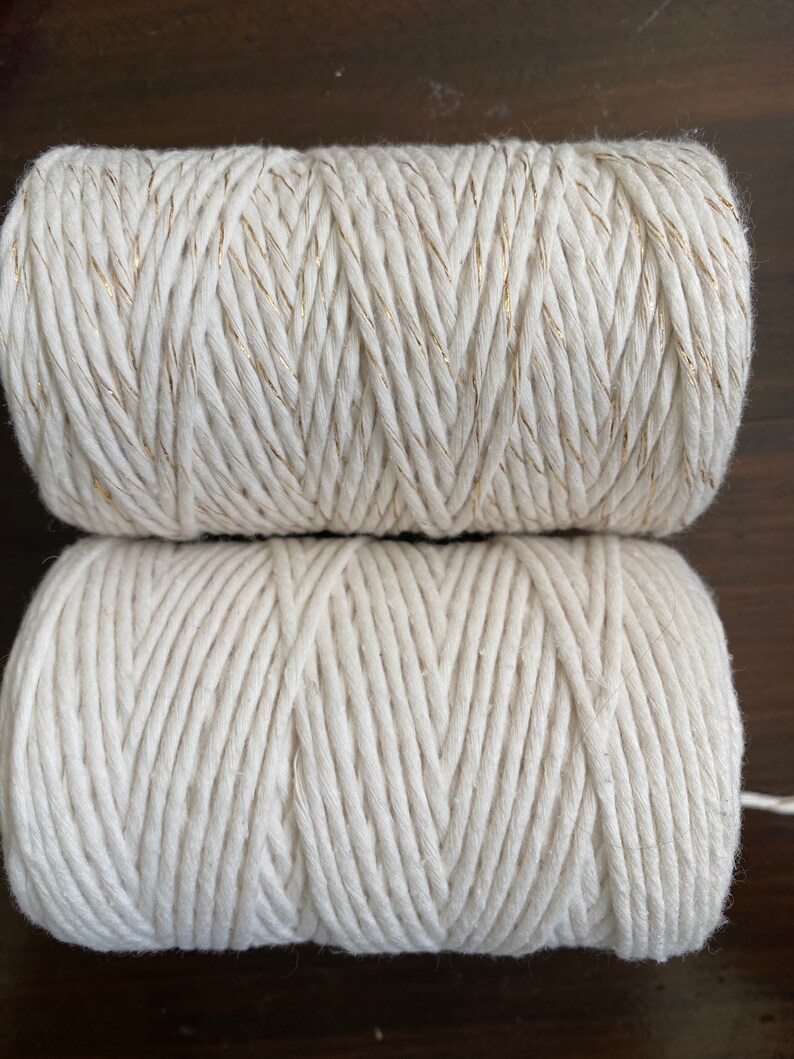 K&ouml;nnte beinhalten: Zwei Spulen aus nat&uuml;rlichem Baumwollseil. Die obere Spule hat einen goldenen Faden, der in das Seil eingewebt ist.