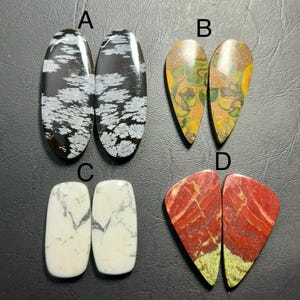 May include: Four pairs of polished gemstone cabochons. Pair A: black with white snowflake patterns. Pair B: teardrop-shaped with green, yellow, and brown patterns. Pair C: white with gray veining. Pair D: red with green and yellow.