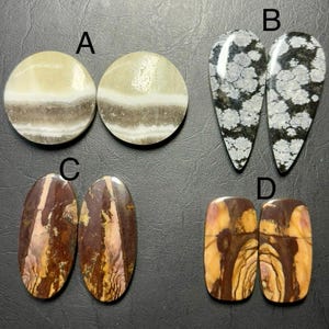 May include: Four pairs of polished gemstones are displayed. Pair A is round with cream, gray, and white bands. Pair B is teardrop-shaped with black and white snowflake patterns. Pair C is oval with brown and pink swirls. Pair D is rectangular with brown and yellow patterns.