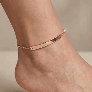 Peut inclure: Une chevillère en or rose composée d'une fine chaîne délicate et d'une plaque horizontale incurvée et lisse. Le centre de la barre métallique est gravé du prénom Alexandra dans une police cursive, offrant une finition métallique polie.