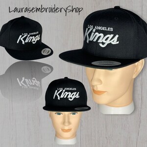 May include: Black and white Los Angeles Kings embroidered baseball cap. The cap has a curved brim and a snap closure.
