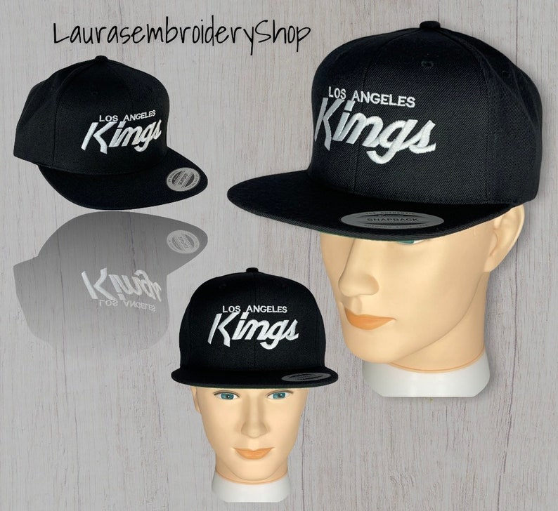 May include: Black and white Los Angeles Kings embroidered baseball cap. The cap has a curved brim and a snap closure.