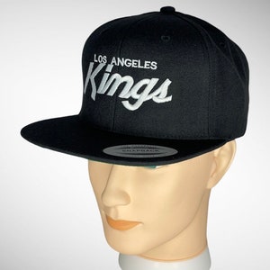 May include: Black baseball cap with a white embroidered Los Angeles Kings logo.