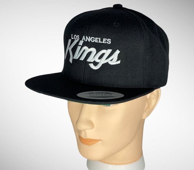 May include: Black baseball cap with a white embroidered Los Angeles Kings logo.