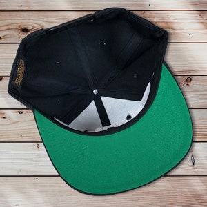 May include: Black and green baseball cap with a black brim and a green crown. The cap is turned inside out, showing the inside of the crown.