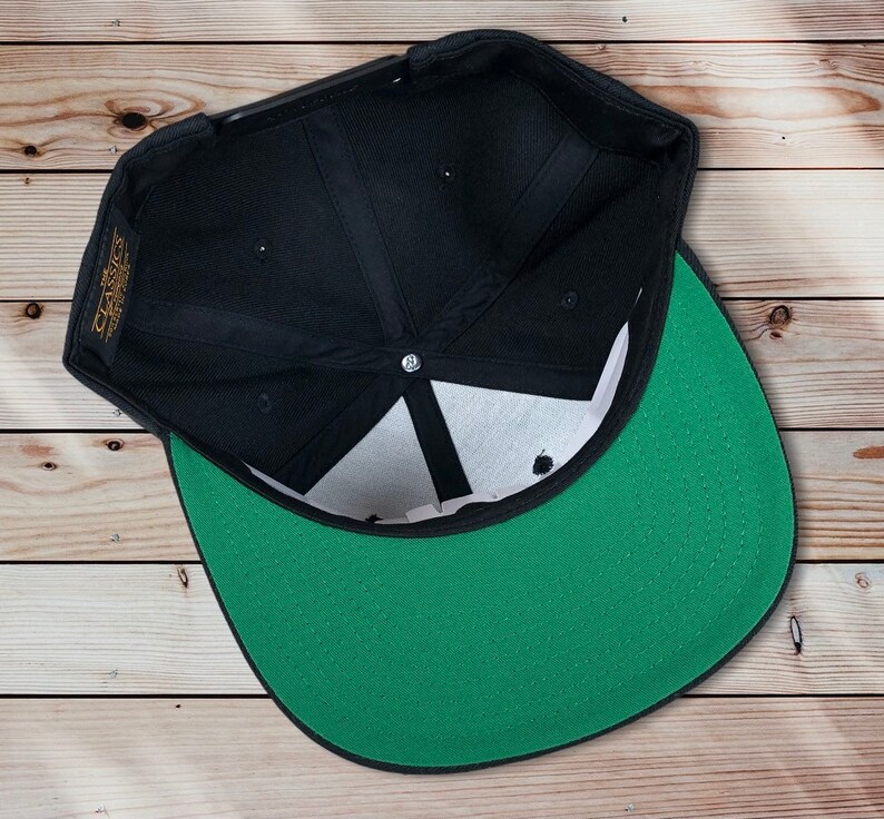 May include: Black and green baseball cap with a black brim and a green crown. The cap is turned inside out, showing the inside of the crown.