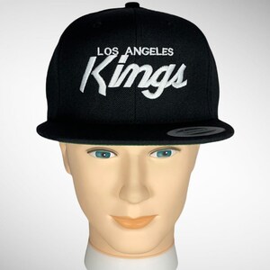 May include: Black baseball cap with a white embroidered Los Angeles Kings logo.