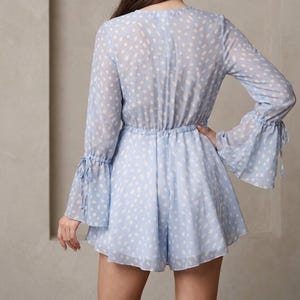 May include: Pale blue romper with white polka dots. It has long sleeves with flared cuffs and tie details. The waist is gathered with a drawstring. The fabric is sheer and lightweight, ideal for warmer weather.