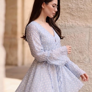 May include: A pale blue dress with white polka dots. The dress has long, sheer sleeves with frilled cuffs and a V-neck. A tie defines the waist, and the skirt flares. The dress is made of a lightweight material.